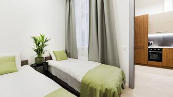A modern hotel room with two beds, a small table with a plant, and a view of the kitchen.