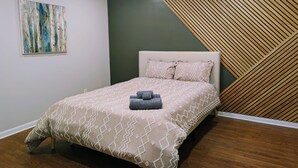Une chambre à coucher comprenant un lit, un ventilateur de plafond, une œuvre d’art accrochée au mur et un mur décoré de lambris en bois.