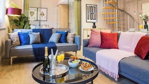 Ein modernes Wohnzimmer mit einem Glastisch, zwei Sofas mit Kissen, einer Wendeltreppe und einem großen Spiegel, der den Raum reflektiert.