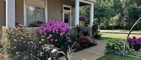 Een huis met een veranda, omringd door een verzorgde tuin met verschillende bloemen en struiken.