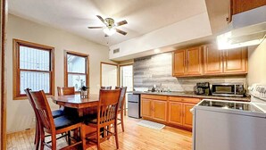 A kitchen with wooden cabinets, a dining table with chairs, a ceiling fan, and a refrigerator. - Enjoy the entire main level of this Historic Victorian duplex form the 1800s. Located in the heart of Cambridge. Unwind in private 4-person sauna, king size beds, quaint front porch and fully stocked kitchen. Walk to everything in town. (Cambridge)