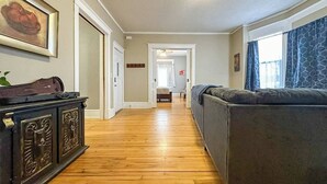 A hallway with a wooden floor, a dark-colored sofa, and a decorative cabinet. - Enjoy the entire main level of this Historic Victorian duplex form the 1800s. Located in the heart of Cambridge. Unwind in private 4-person sauna, king size beds, quaint front porch and fully stocked kitchen. Walk to everything in town. (Cambridge)