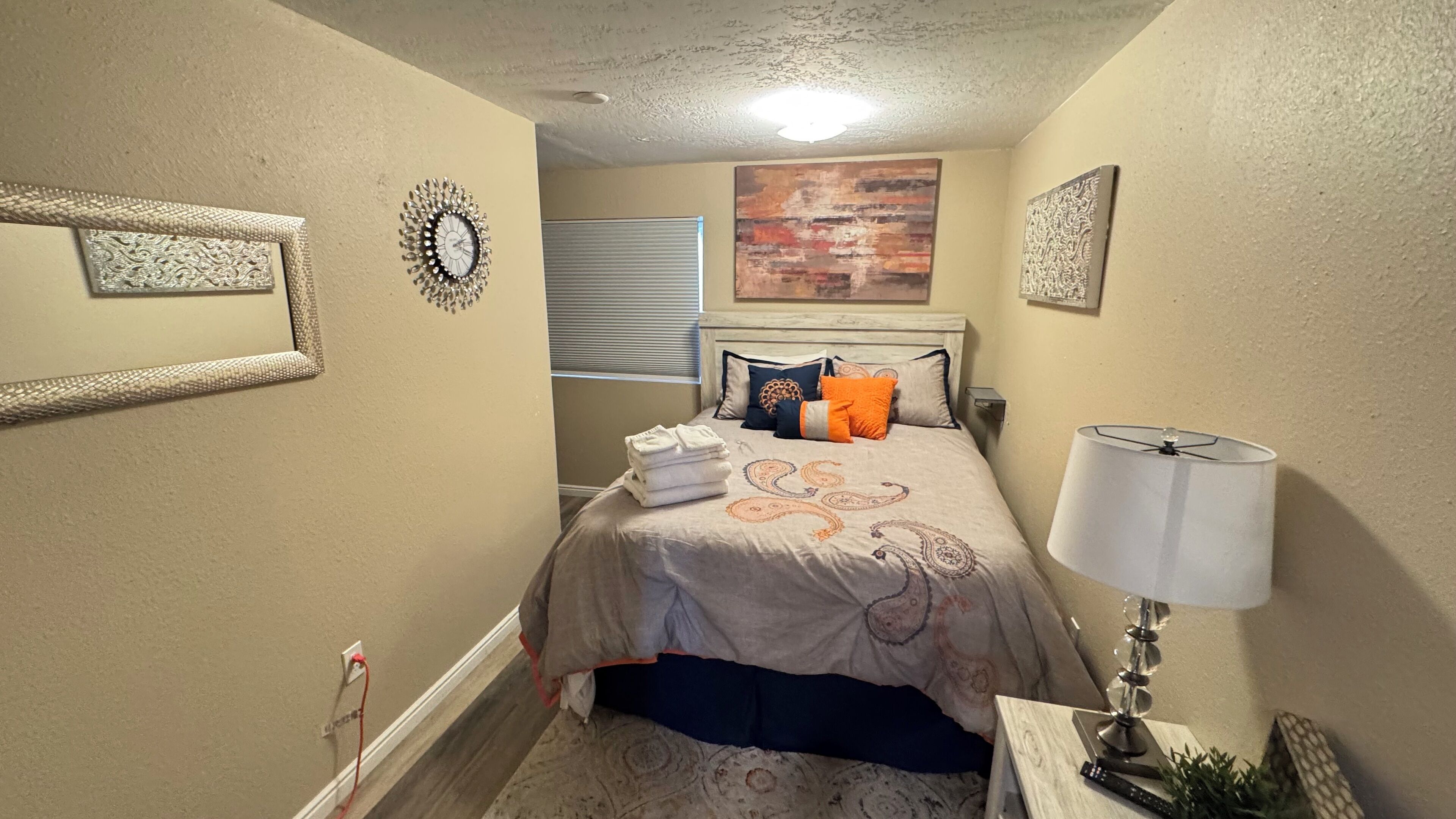 Un dormitorio con cama, almohadas, una lámpara y un reloj de pared.