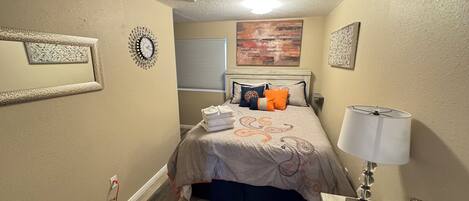Un dormitorio con cama, almohadas, una lámpara y un reloj de pared.