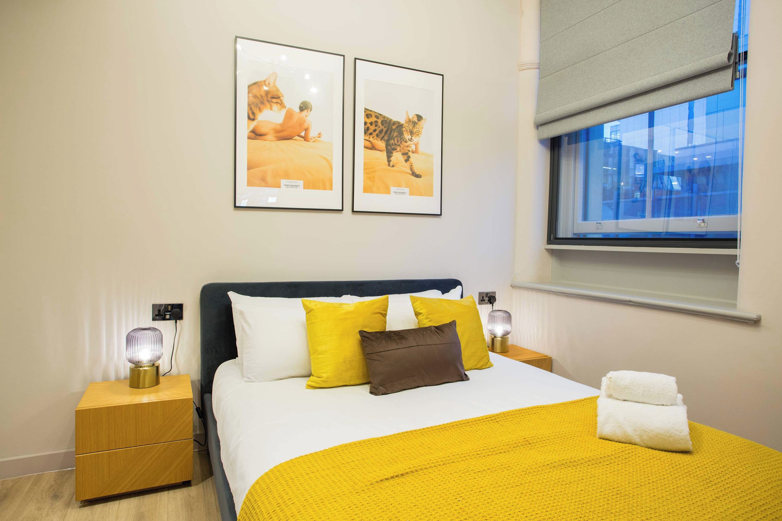 Ein Hotelzimmer mit einem Bett, zwei Nachttischen, einem Fenster mit Blick und zwei gerahmten Bildern an der Wand.