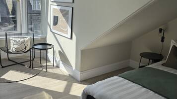 A bedroom with a bed, a chair, a small table, and a window with a view of buildings.