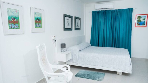 Une chambre à coucher avec un lit, un fauteuil à bascule blanc et des œuvres d’art accrochées au mur.