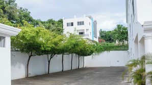 Un espace de stationnement bordé d’une rangée d’arbres, avec un bâtiment blanc en arrière-plan.