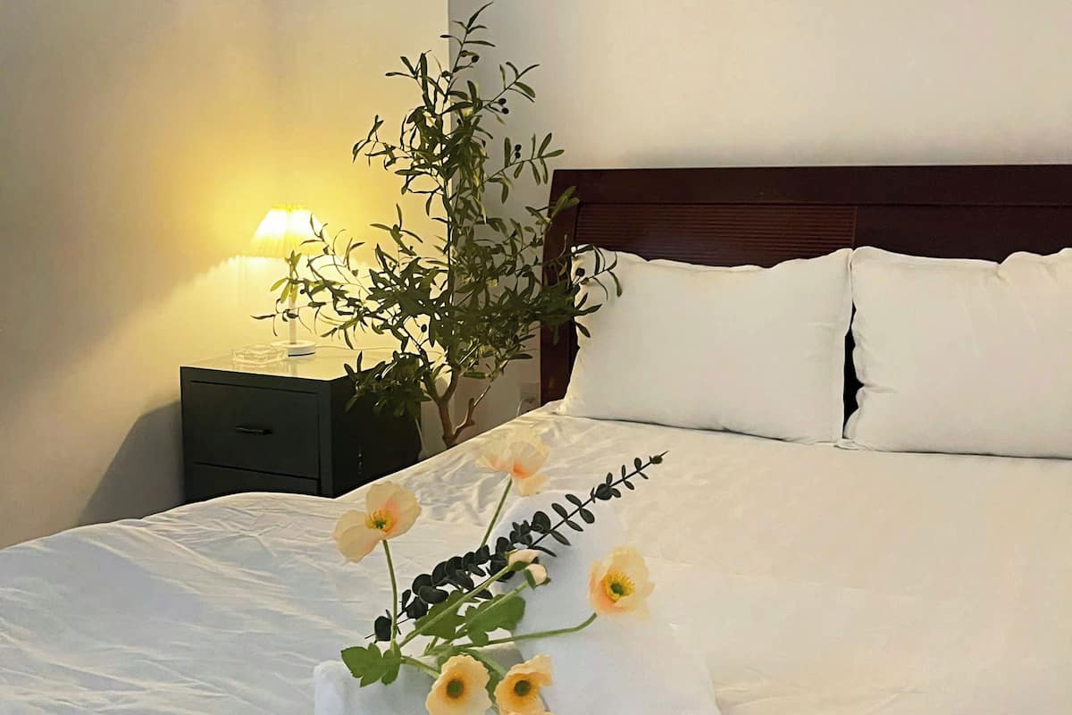 Een opgemaakt bed met witte lakens, een opgerolde handdoek en een bloemstuk.