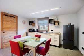 Una cocina compacta con una mesa de comedor, sillas, un refrigerador y una ventana con persianas.