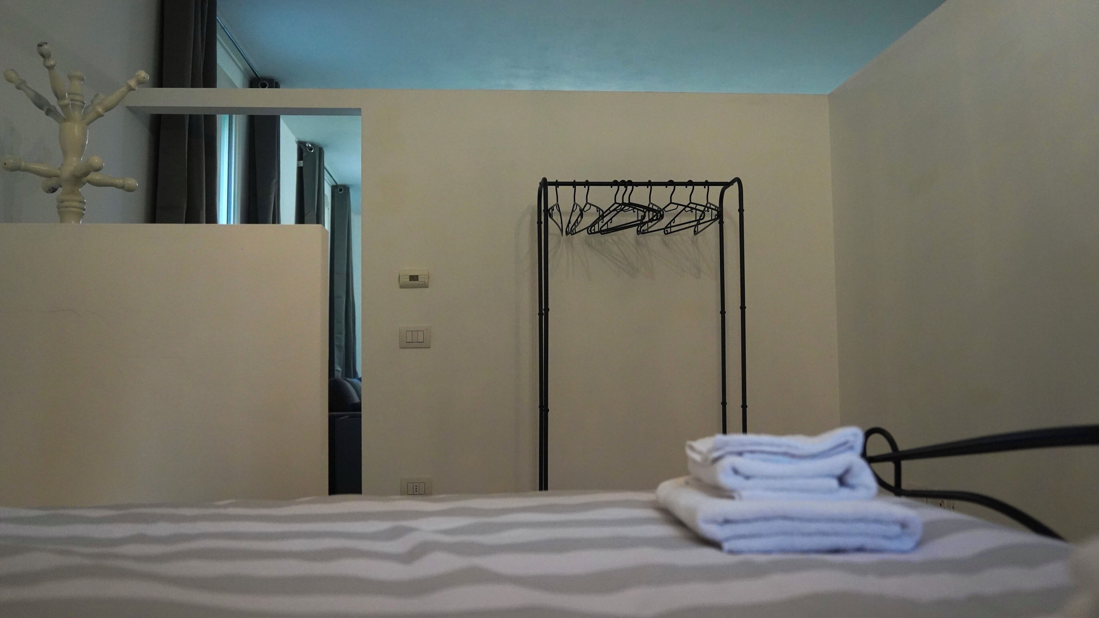 Une chambre d’hôtel avec un lit, un étendoir fixé au mur et une porte donnant sur une autre pièce.
