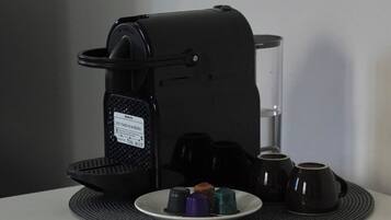 En kaffemaskin med en uppsamlingsbricka, ett glas vatten och en tallrik med kaffekoppar och en kaffekapsel.