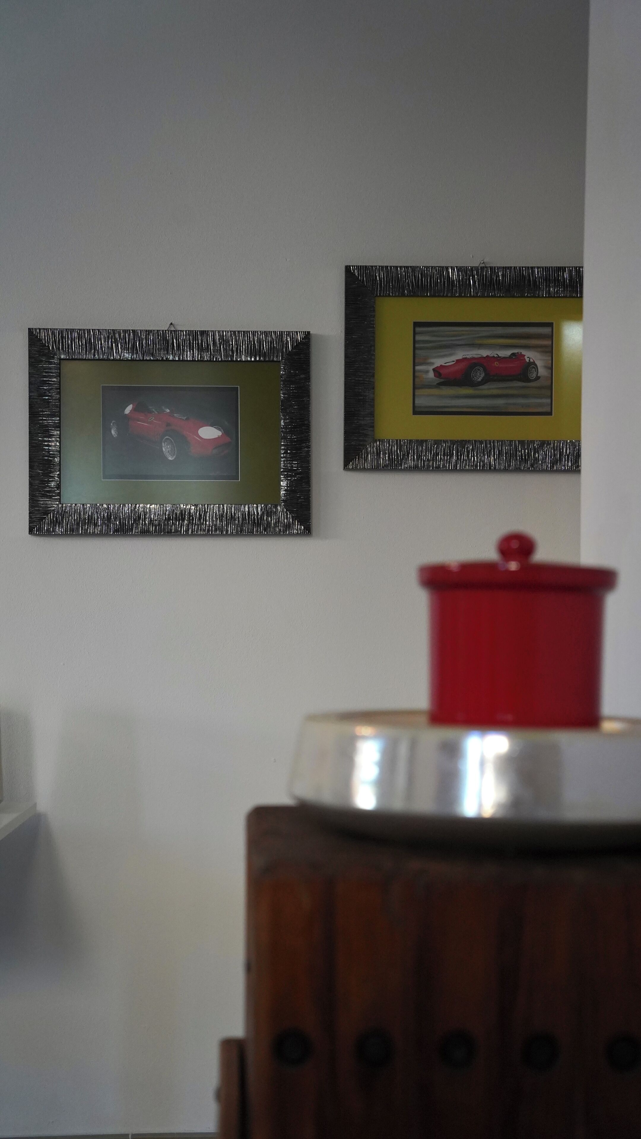 Une pièce avec deux tableaux encadrés accrochés au mur, un objet rouge au premier plan et un meuble en bois.