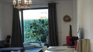 Un salon moderne comprenant un coin repas, un lustre, une vue sur la verdure et une machine à café.