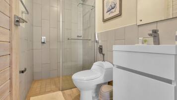 Un baño moderno con ducha de vidrio, inodoro blanco y lavamanos con espejo.