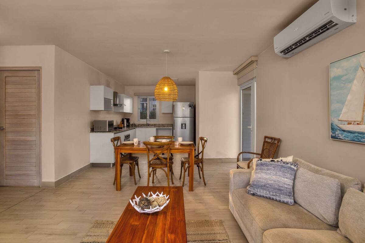 Una sala de estar moderna con una mesa de centro de madera, un sofá beige y una zona de comedor con sillas de madera y una mesa blanca.