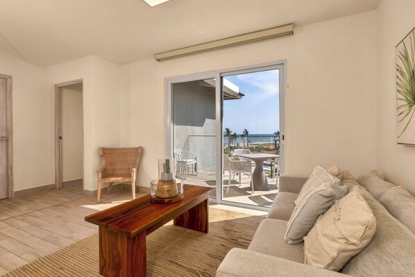 A modern living room with a wooden coffee table, a beige sofa, and a view of the ocean through a sliding glass door. - Villas Residences by Playa Caracol Resorts (Punta Chame)