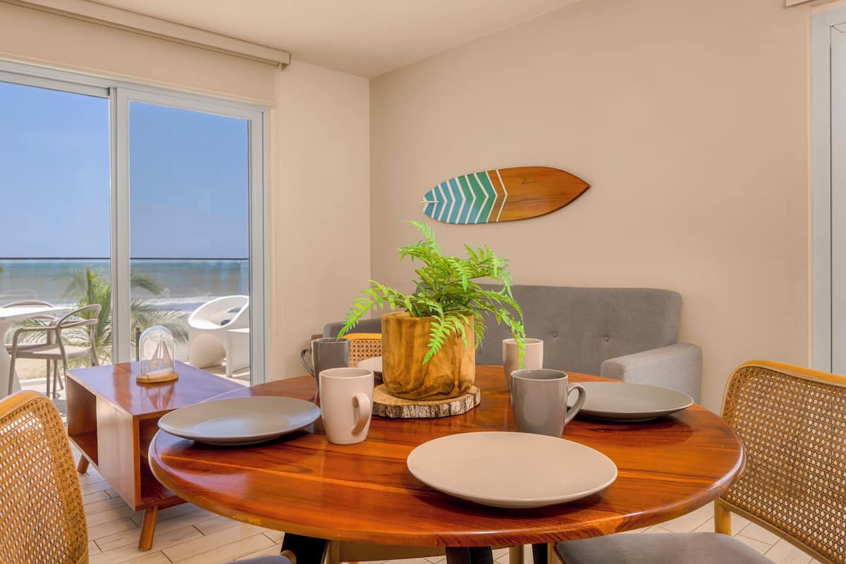 Un comedor con una mesa de madera, platos blancos y una planta en maceta.
