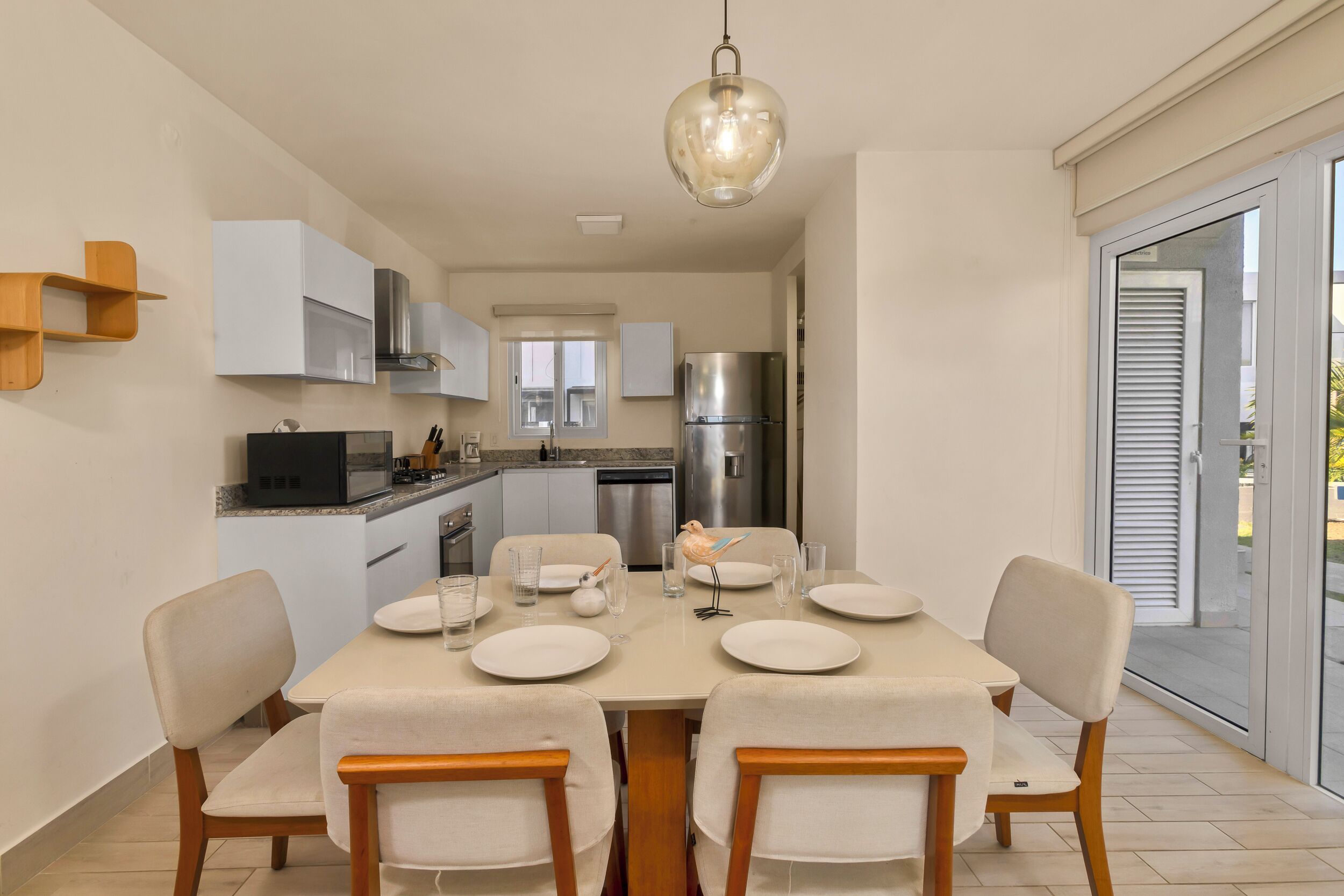 Une cuisine moderne avec des meubles blancs, un réfrigérateur en acier inoxydable et un coin repas avec une table dressée pour quatre personnes.