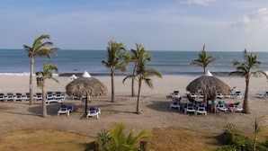 Una playa con sombrillas de paja, palmeras y tumbonas.