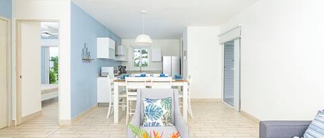 A modern living room with a grey sofa, a dining area with a white table and chairs, and a kitchen in the background.