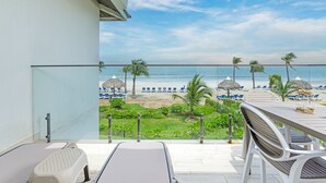 Un balcón con vista a una playa, sillones de descanso y una mesa.
