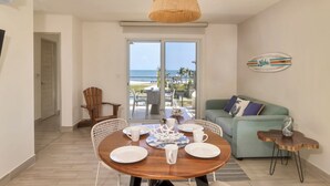 Comedor con mesa de madera dispuesta para cuatro, una lámpara colgante de mimbre y vista al océano a través de un ventanal.