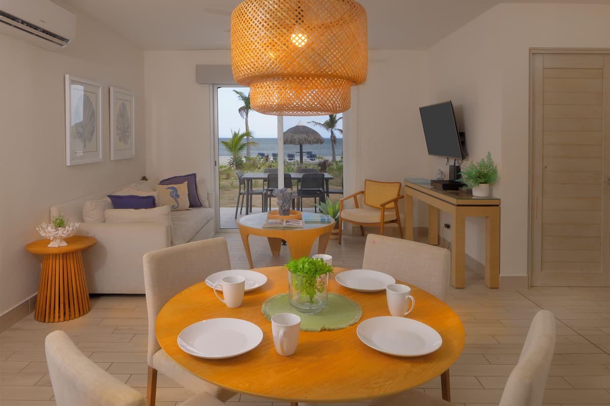 Una sala de estar moderna con comedor, televisor y vista a la playa.