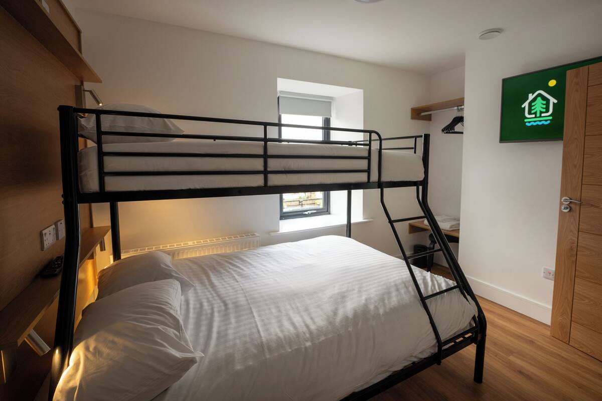 A bunk bed room with a window, a radiator, and a green sign on the wall.