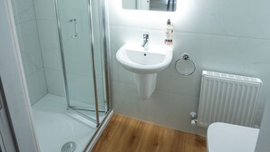 Een badkamer met een douchecabine van glas, een wit wastafelmeubel met een spiegel erboven en een wit toilet.