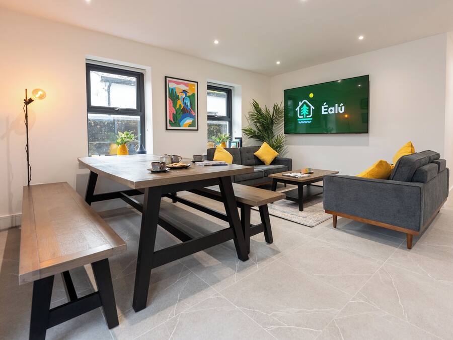 A modern living room with a dining table, sofa, and a TV displaying a logo.