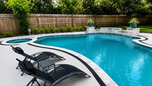 Una piscina de borde curvo, rodeada por un deck de piedra y una valla de madera.