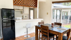 Una cocina moderna con un refrigerador Galanz negro, armarios blancos, un panel divisor de madera y una zona de comedor con una mesa y sillas de madera.