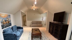 Una sala de estar con un sofá azul, una mesa de centro de madera, un sofá color beige, un armario de madera oscura y un televisor de pantalla plana.