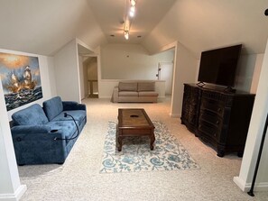 Un salon avec un canapé bleu, une table basse en bois, un canapé beige, un meuble en bois foncé et un téléviseur à écran plat.