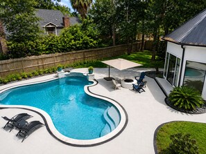 A backyard with a swimming pool, a fire pit, outdoor furniture, and a wooden fence.