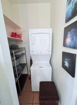 A laundry room with a white washing machine and dryer, shelves with folded clothes, and artwork on the walls.