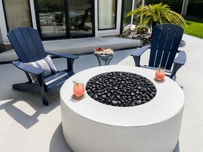 Un espace de détente extérieur moderne, avec deux fauteuils Adirondack, un foyer rond et deux boissons posées sur des dessous de verre.