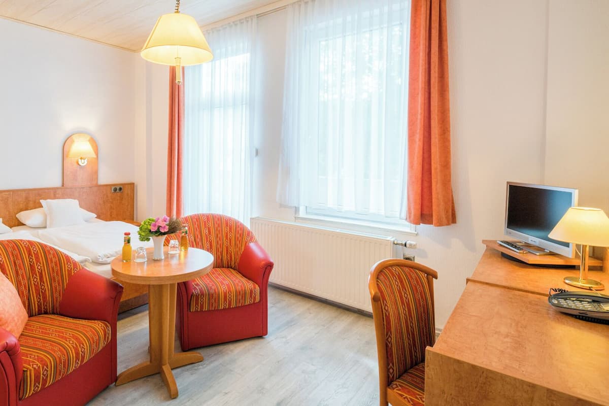 Ein Hotelzimmer mit zwei Betten, einem Esstisch mit Stühlen, einem Fernseher und einem Fenster mit Vorhängen.