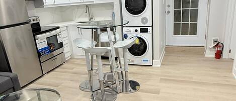 A modern kitchen with white cabinets, stainless steel appliances, a glass table, and a built-in washing machine.