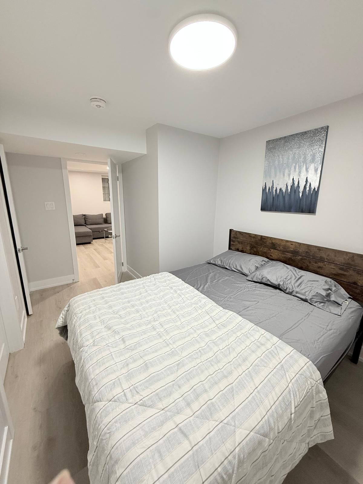 A bedroom with a bed, a headboard, a painting, and a door leading to another room.