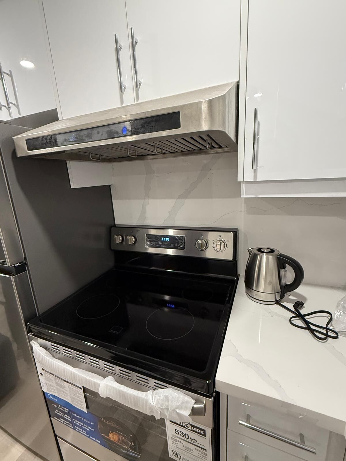 A kitchen with a stainless steel stove, a range hood, and a kettle on the countertop.