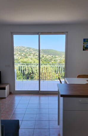 Una habitació amb un gran finestral corredís que dona a un balcó amb vista a un paisatge amb turons.