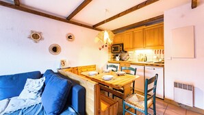 Ein gemütlicher Wohnraum mit Esstisch aus Holz, blauem Sofa und einer Küchenzeile mit Holdekor.