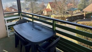 A balcony with a table and chairs, overlooking a village with houses and mountains. - Cozy apartment with lake view (Gérardmer)