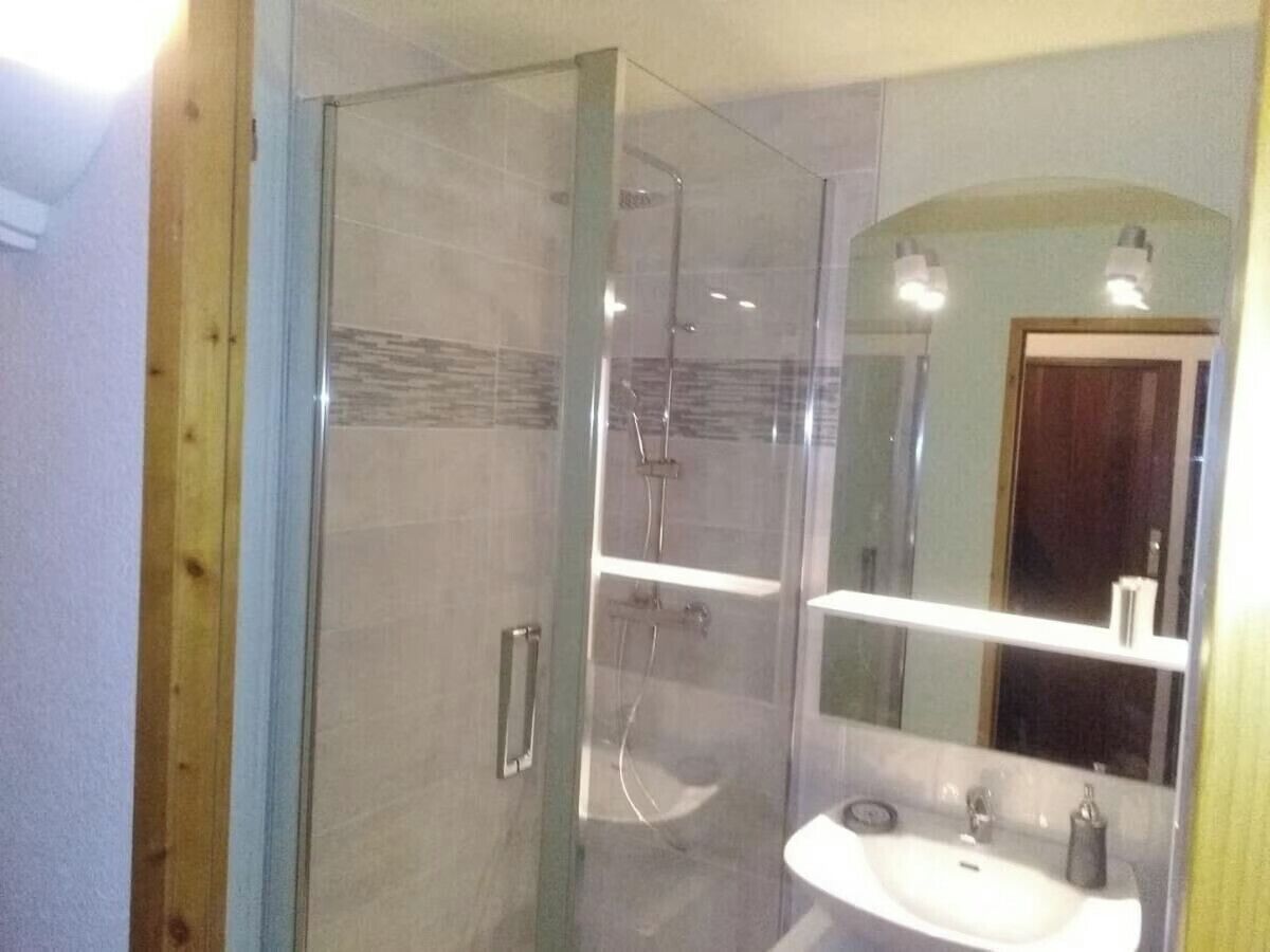 Een douche met glazen wand, een handdouche, een wastafel met spiegel en een handdoekrek.
