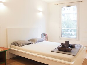 A minimalist bedroom with a bed, a small bedside table, a window, and a framed picture on the wall. - Charming, bright studio in the heart of Paris (Paris)