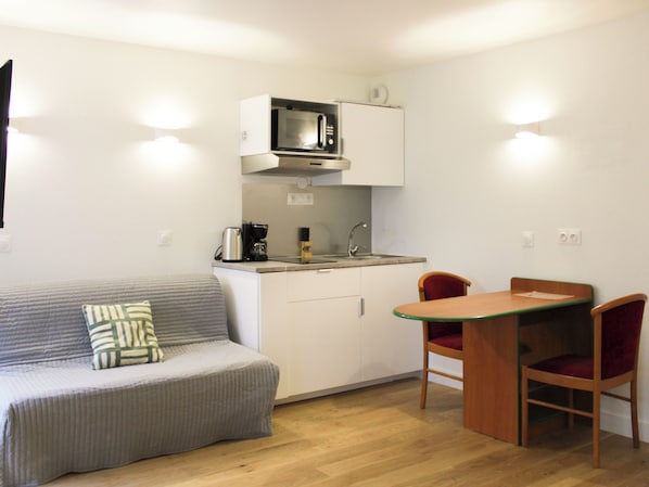 A compact kitchenette with a microwave, coffee maker, and sink. There's a small dining table with two chairs and a sofa with a cushion. - Charming, bright studio in the heart of Paris (Paris)
