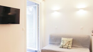A room with a sofa, a television mounted on the wall, and a sliding glass door leading to an outdoor area. - Charming, bright studio in the heart of Paris (Paris)