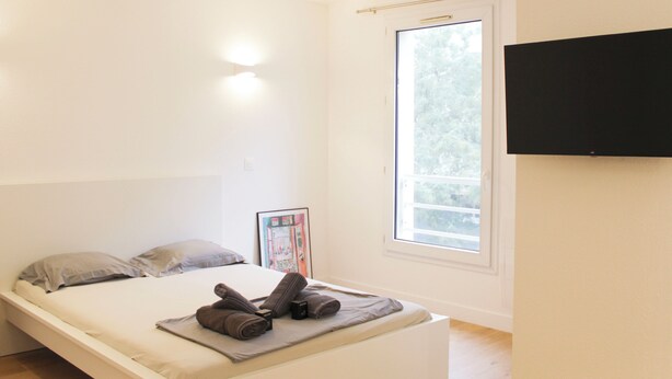 A minimalist bedroom with a bed, a window, and a flat-screen TV mounted on the wall. - Charming, bright studio in the heart of Paris (Paris)
